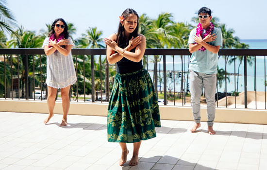 Man and woman taking a hula lesson on a terrace overlooking the ocean.
