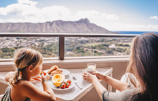 Mother and daughter having breakfast on a balcony overlooking Diamond Head in Waikiki.