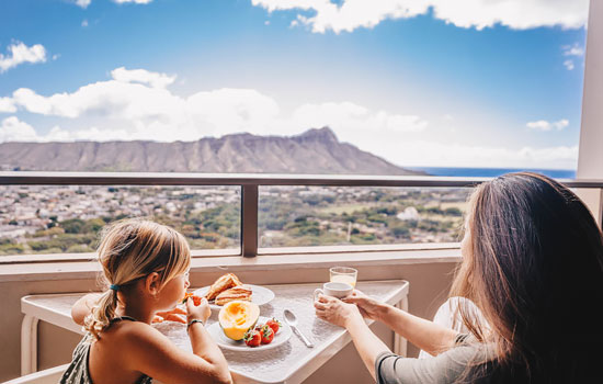 Mother and daughter having breakfast on a balcony overlooking Diamond Head in Waikiki.