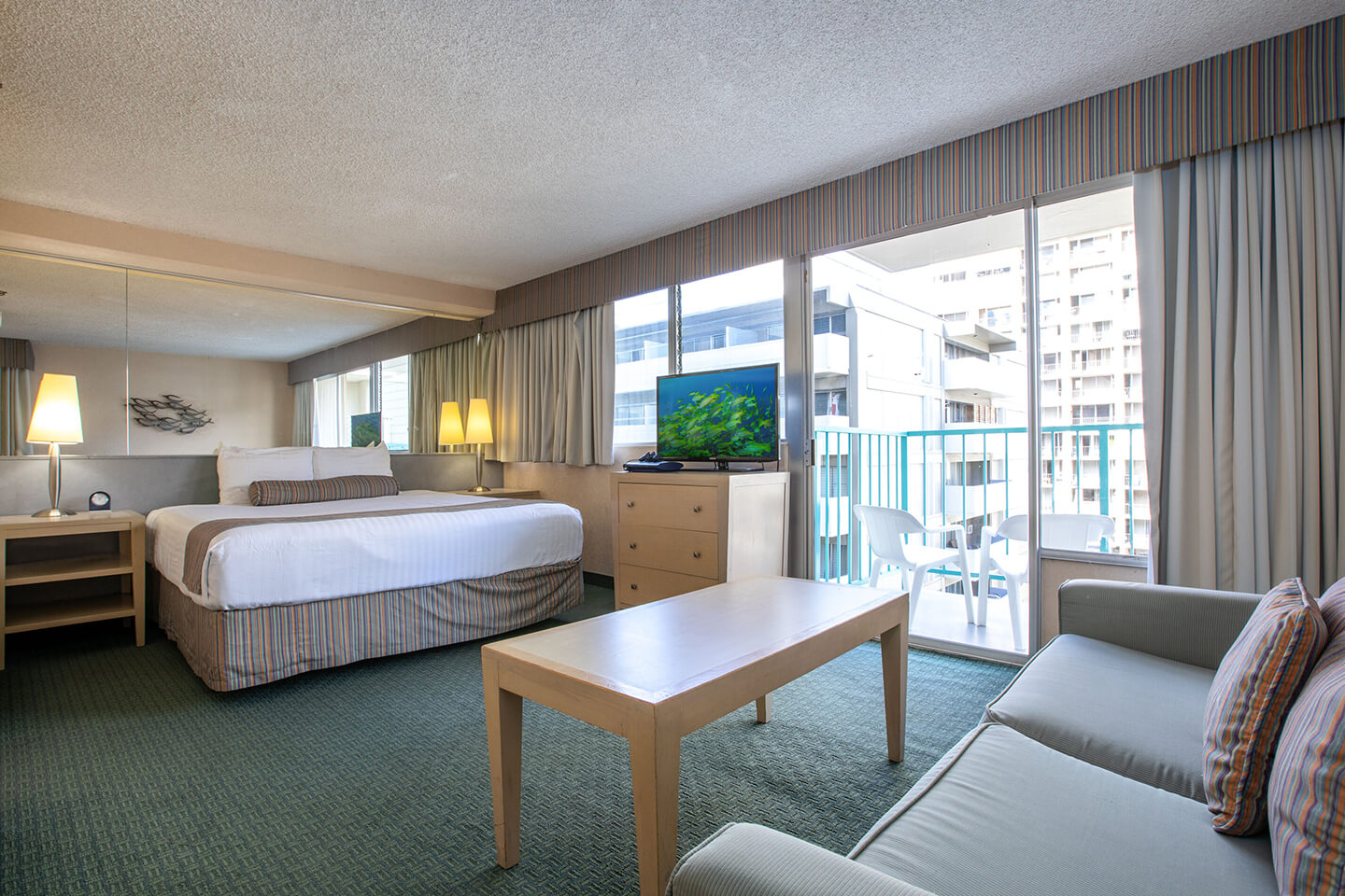 Room with a bed, nightstand, TV, coffee table, couch, and balcony.