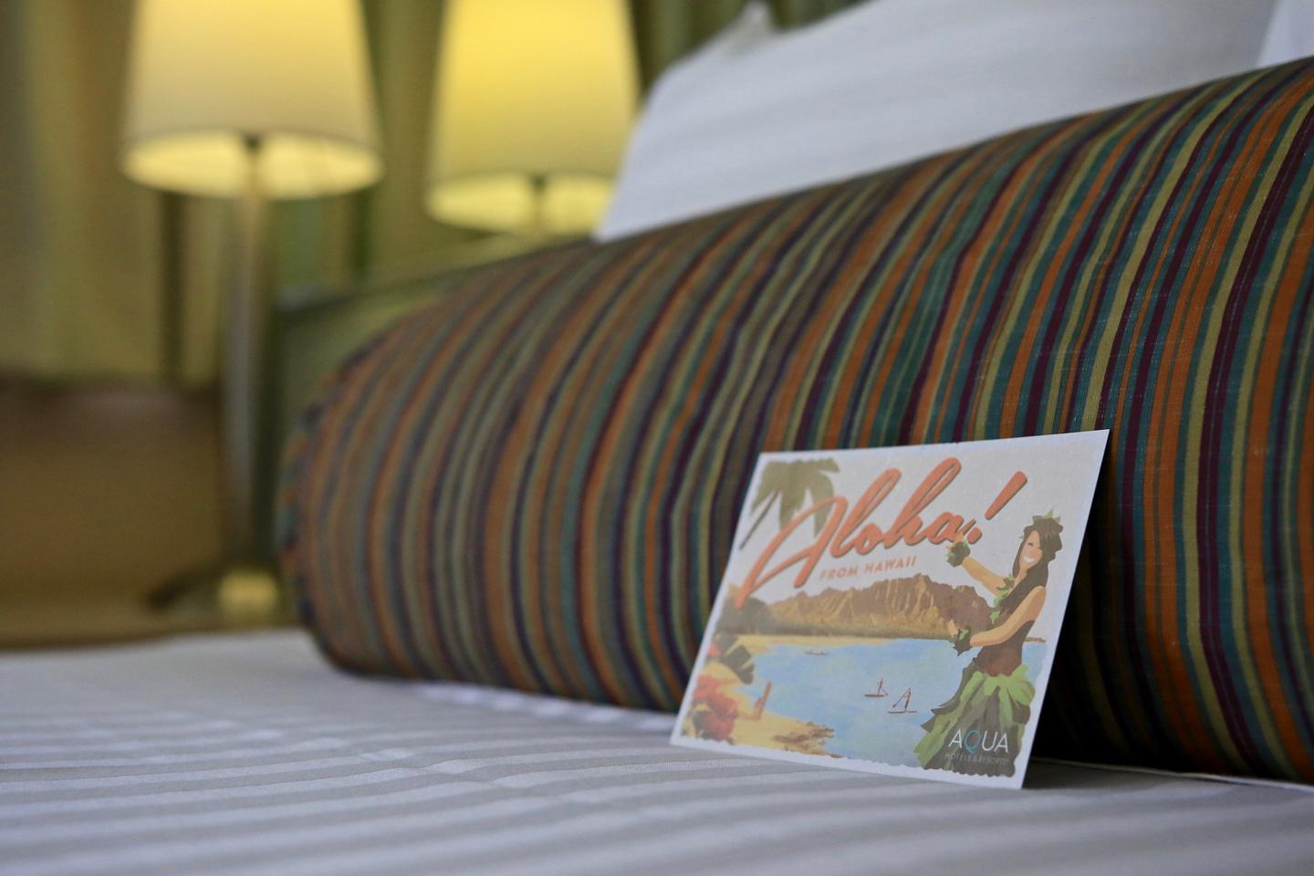Pillow on bed and Aloha postcard.