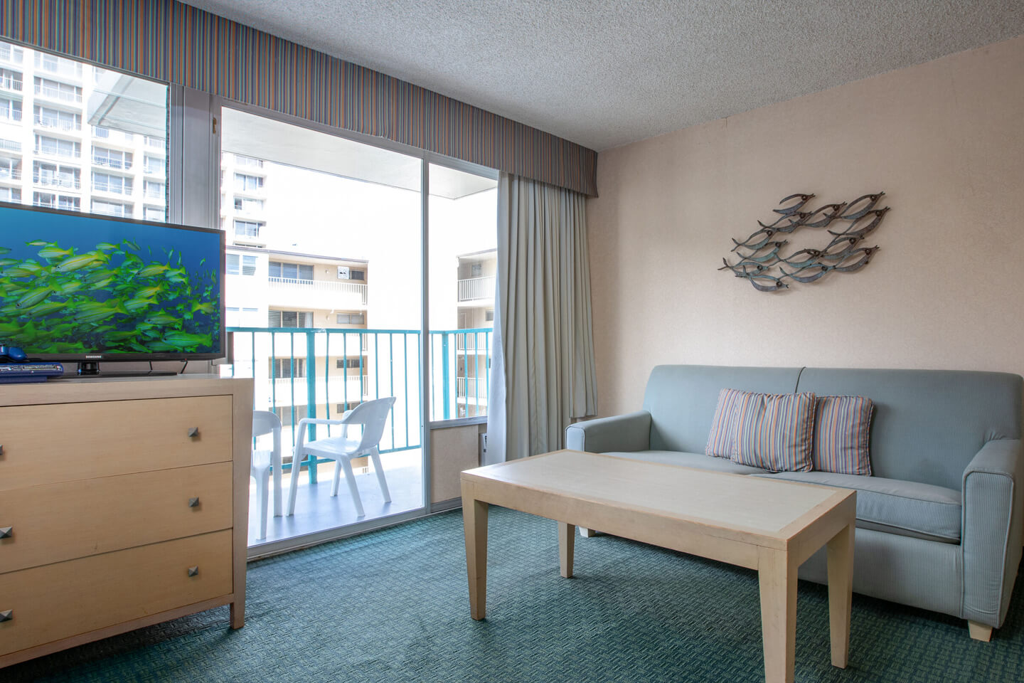 Living area with TV on dresser, coffee table, couch, and balcony.
