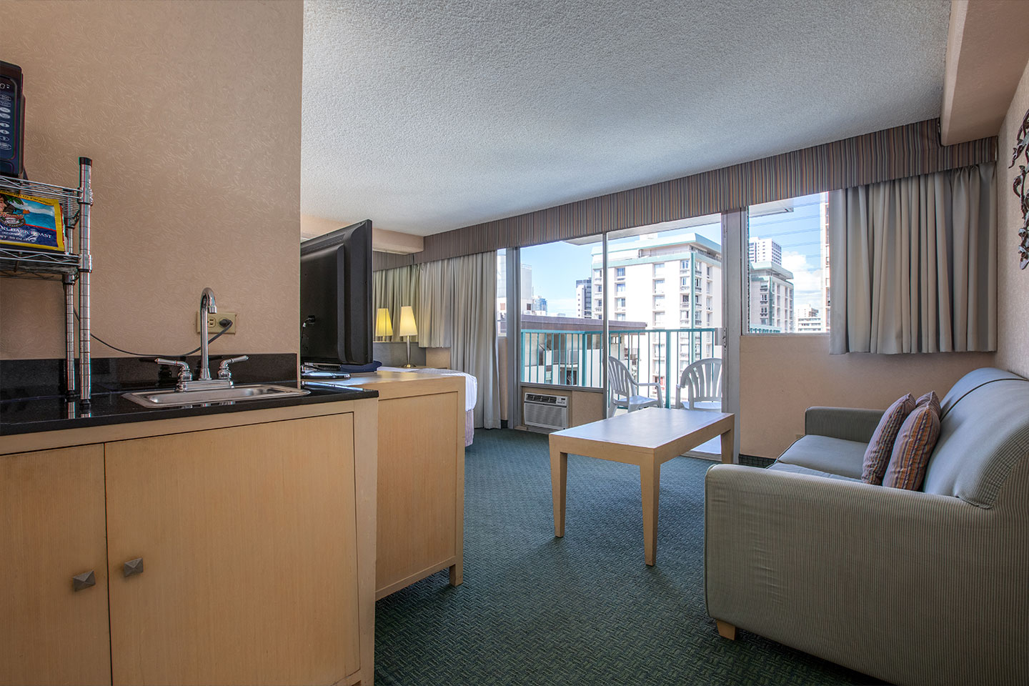 Wet bar area with a sink and room with a bed, TV, coffee table, couch, and balcony.