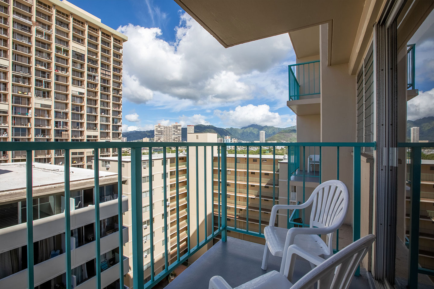 Balcony with 2 chairs and small table with view of buildings and mountain.