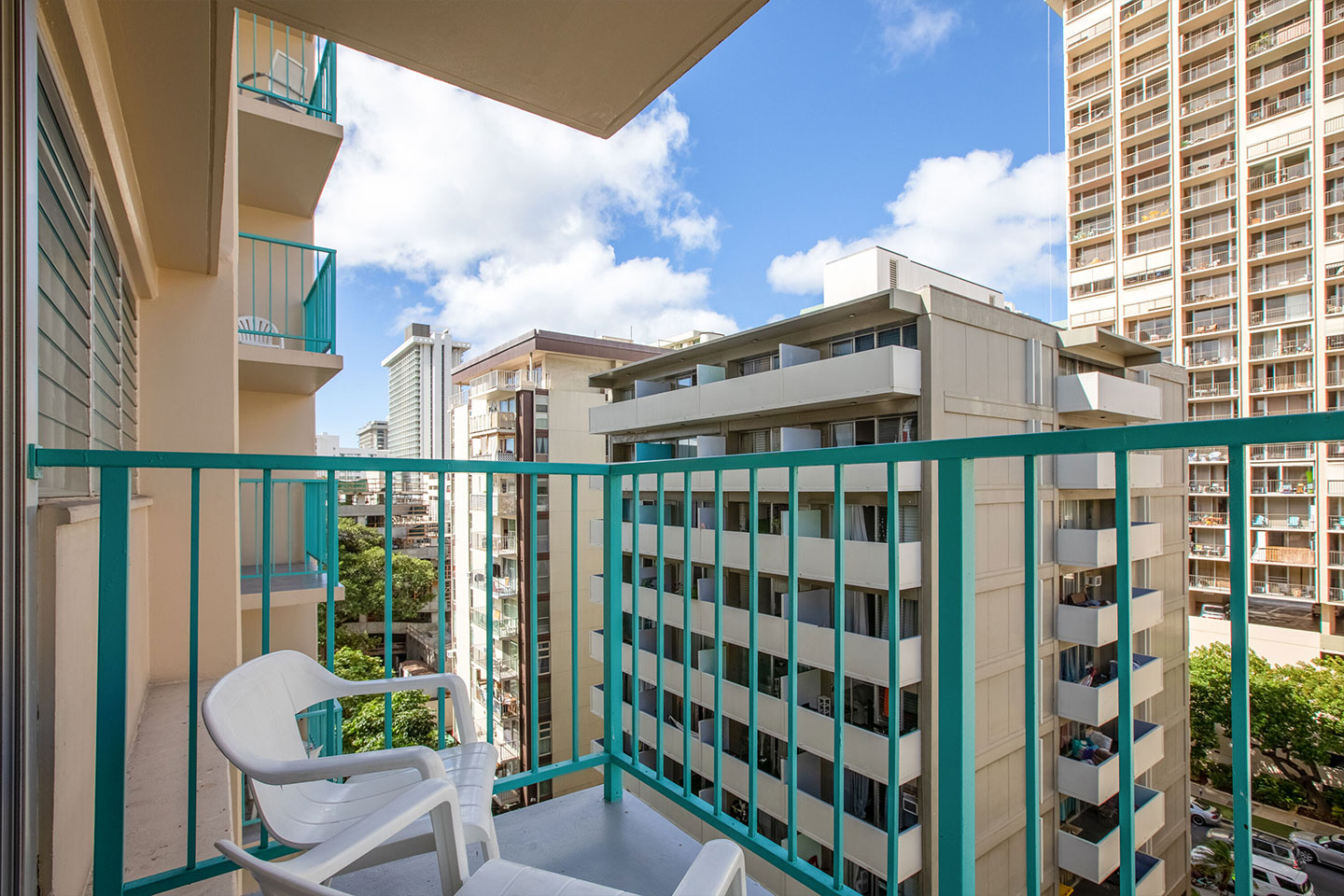 Balcony with 2 chairs and small table with view of street and buildings.