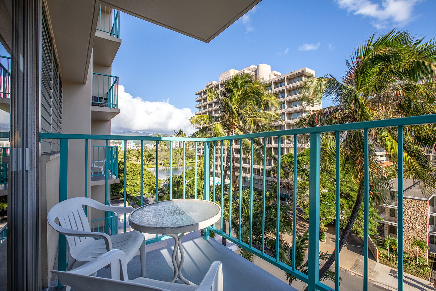 Balcony with 2 chairs and small table with view of street and buildings.
