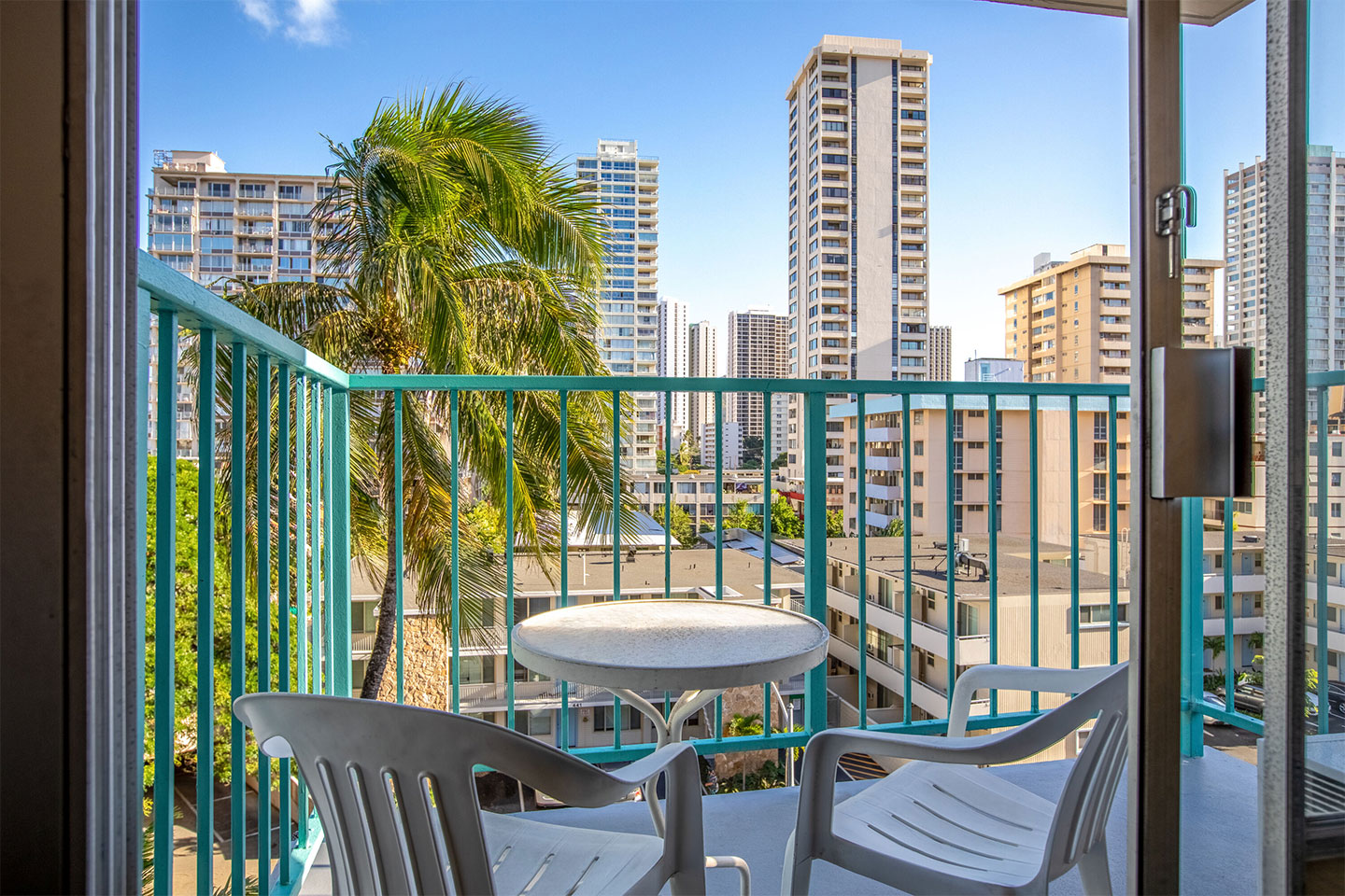 Balcony with 2 chairs and small table with view of street and buildings.