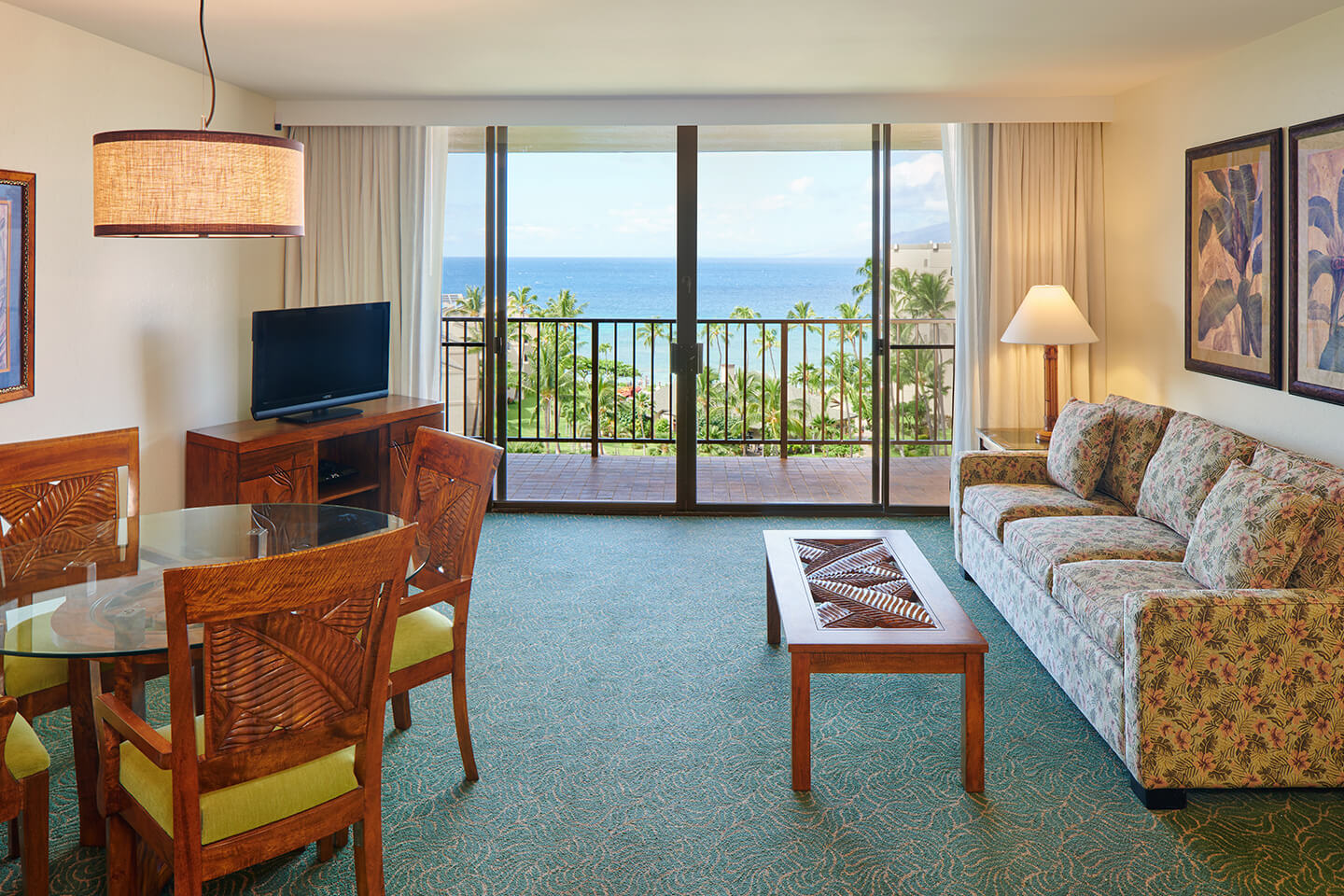 Living area with a couch, coffee table, TV, dining area, and balcony with ocean view.