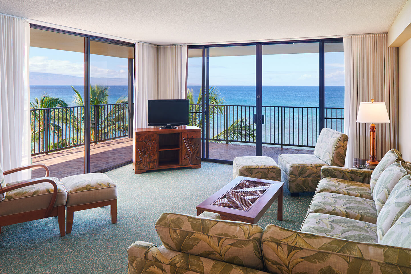 Living area with a couch, coffee table, TV, lamps, and balcony with ocean views.