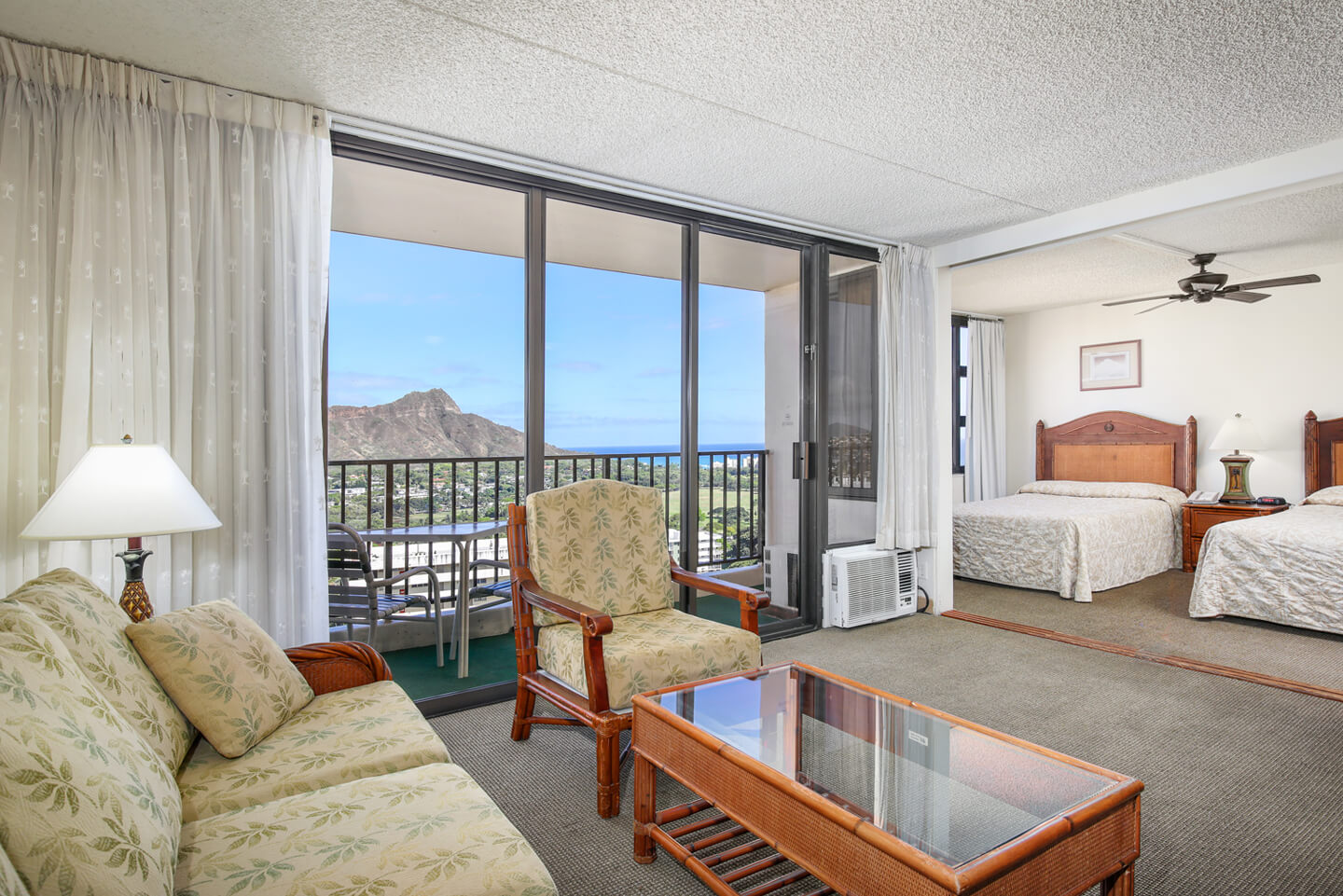 Living area with a couch, coffee table, TV, balcony, and entryway to bedroom.