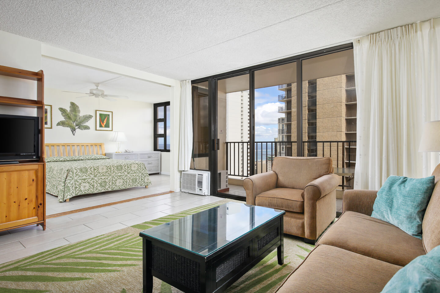 Living room with a couch, coffee table, TV, balcony, and entryway to bedroom.