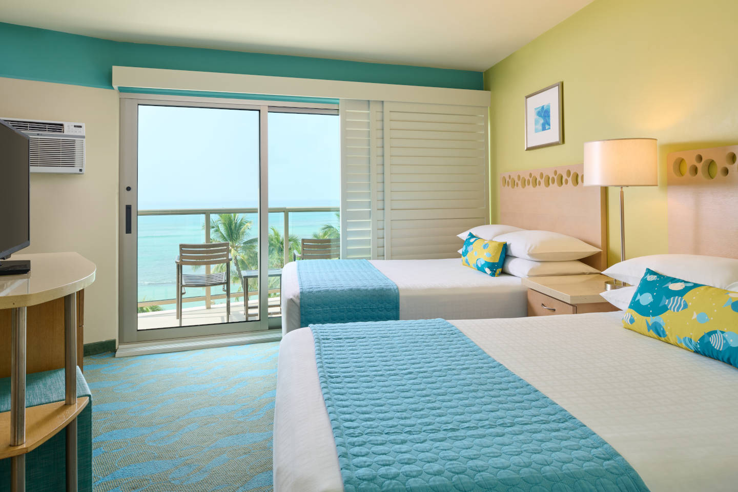 Room with 2 beds, nightstand, lamps, dresser, TV, and balcony with oceanfront view.