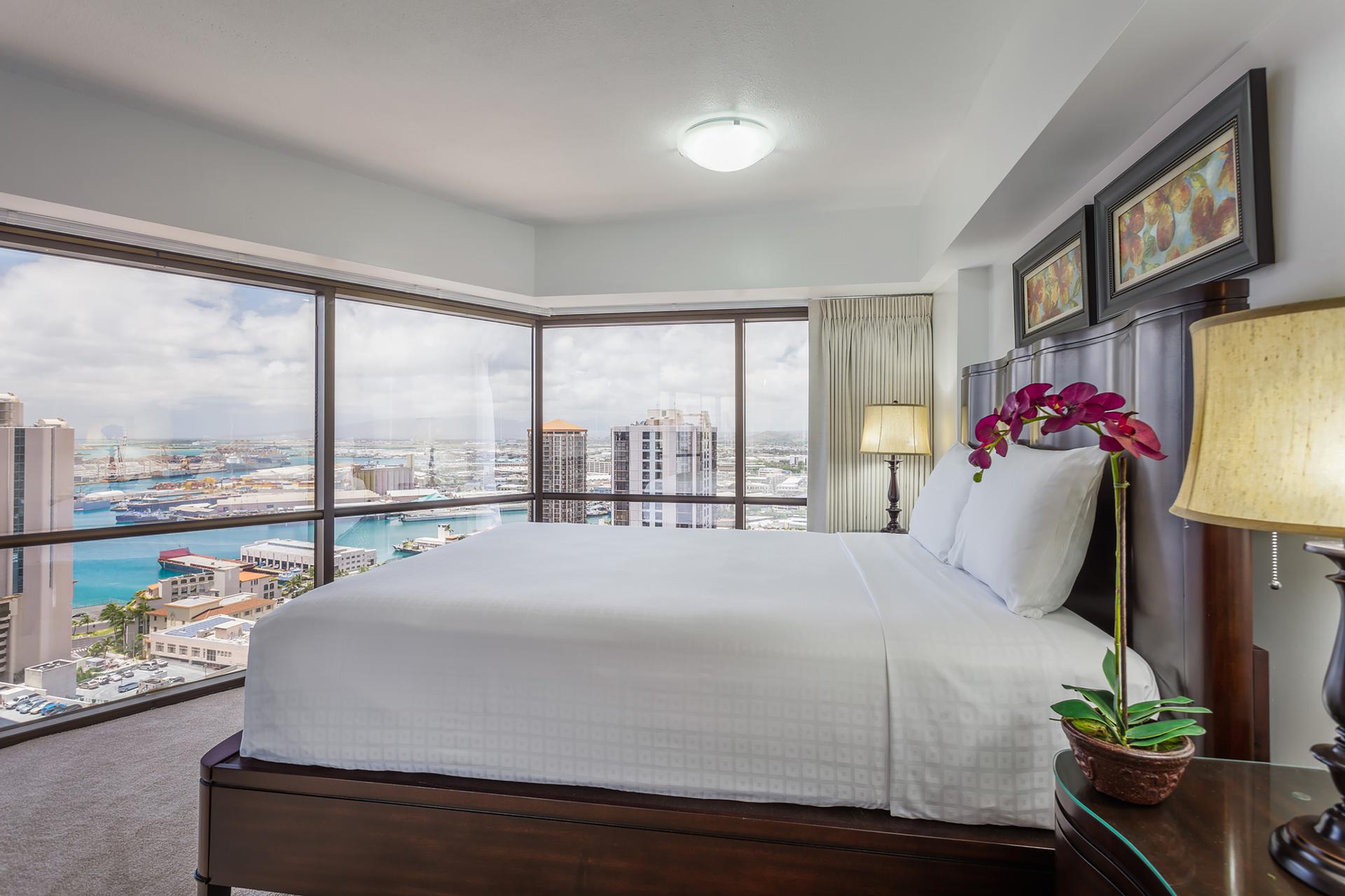 Room with large windows and view of ocean, a bed, nightstand, and lamps.