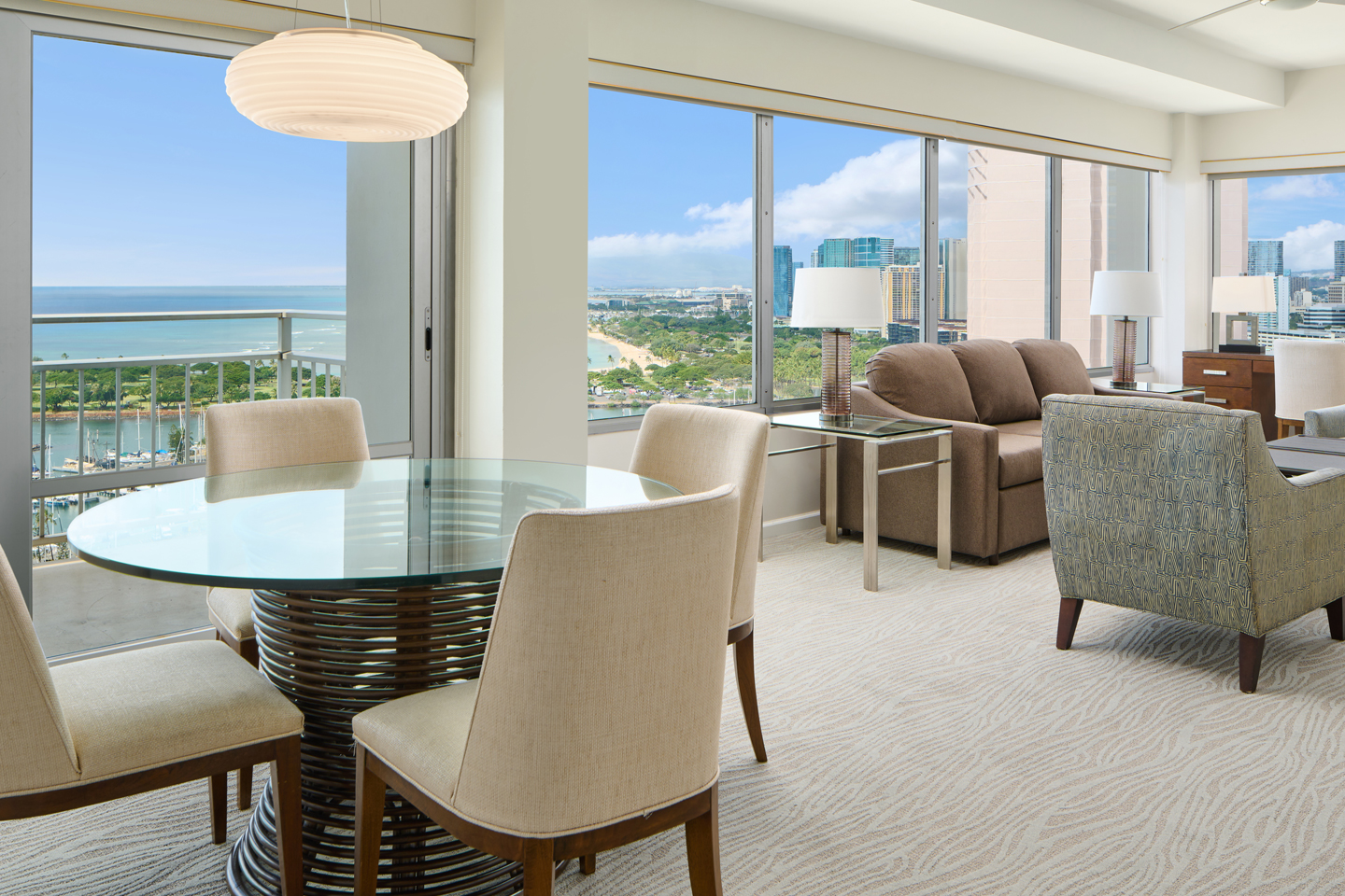 Living area with dining table, couch, chairs, large picture windows. and balcony.