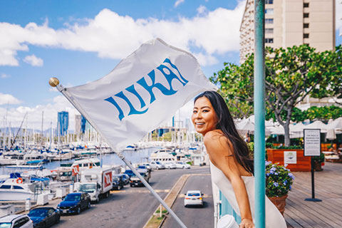 Woman enjoying view of harbor, IKILAI flag flying above.