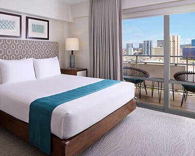 Room with a bed, nightstands, lamps, couch and balcony.