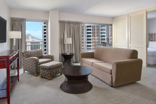 Living room area with a sofa, a comfy chair, coffee table and light fixtures in two bedroom ocean view suite 