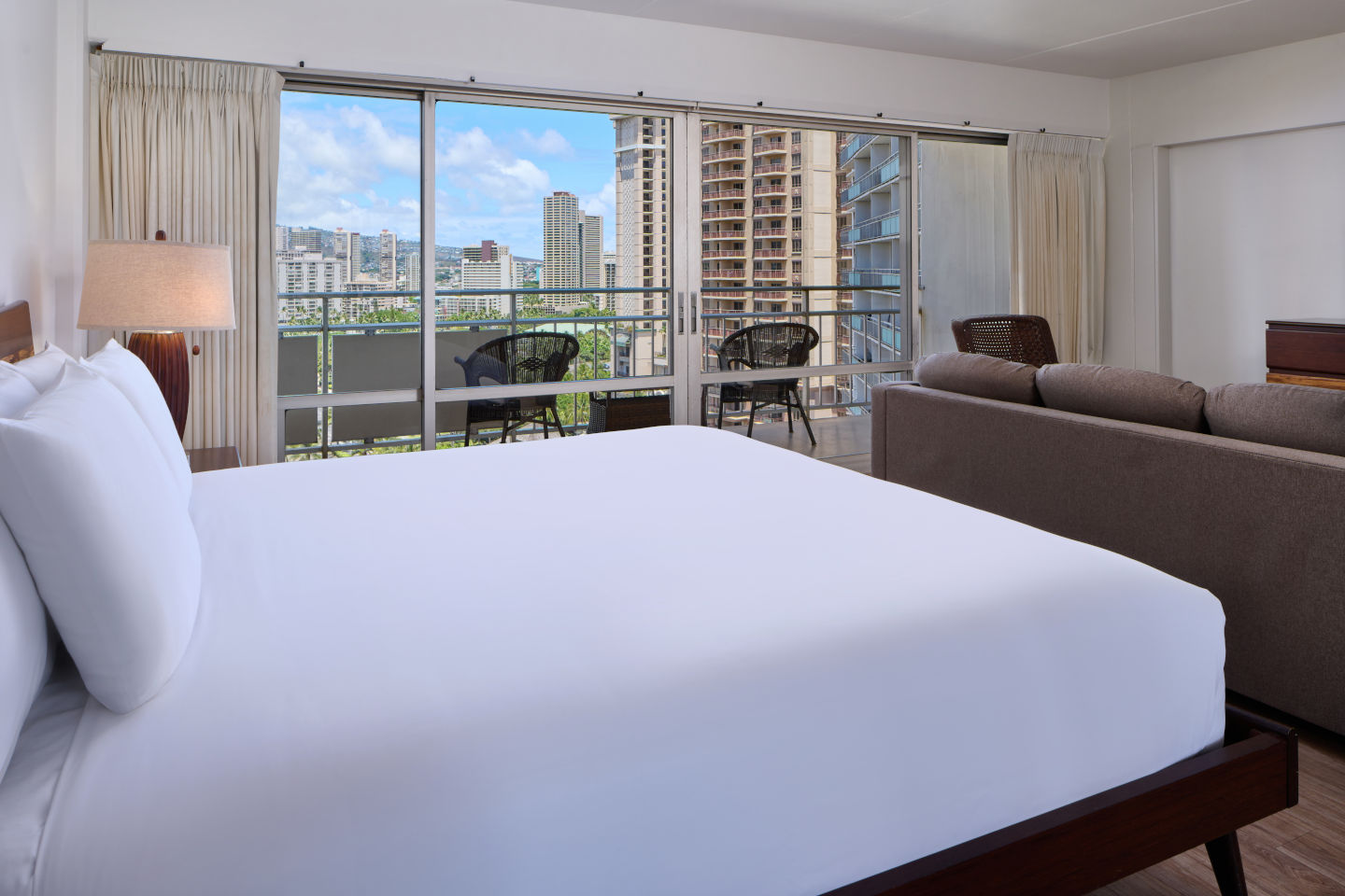 Room with a bed, couch, lamp, and balcony with chairs and table.