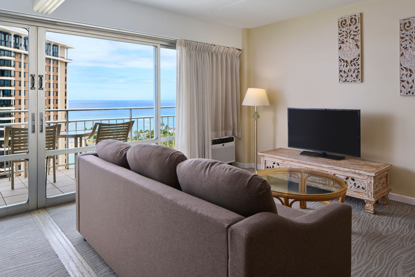 Living area with a couch, coffee table, TV, lamp, and balcony with ocean view.
