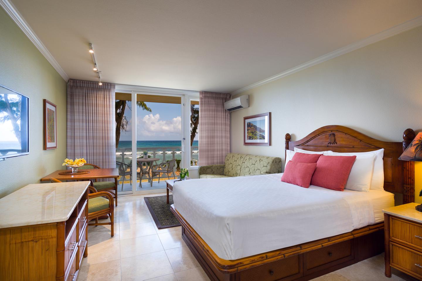 Room with a bed, night stand, lamps, dining area, couch, and balcony with oceanfront view.