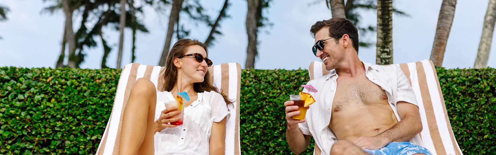 Couple relaxing with drinks on pool loungers