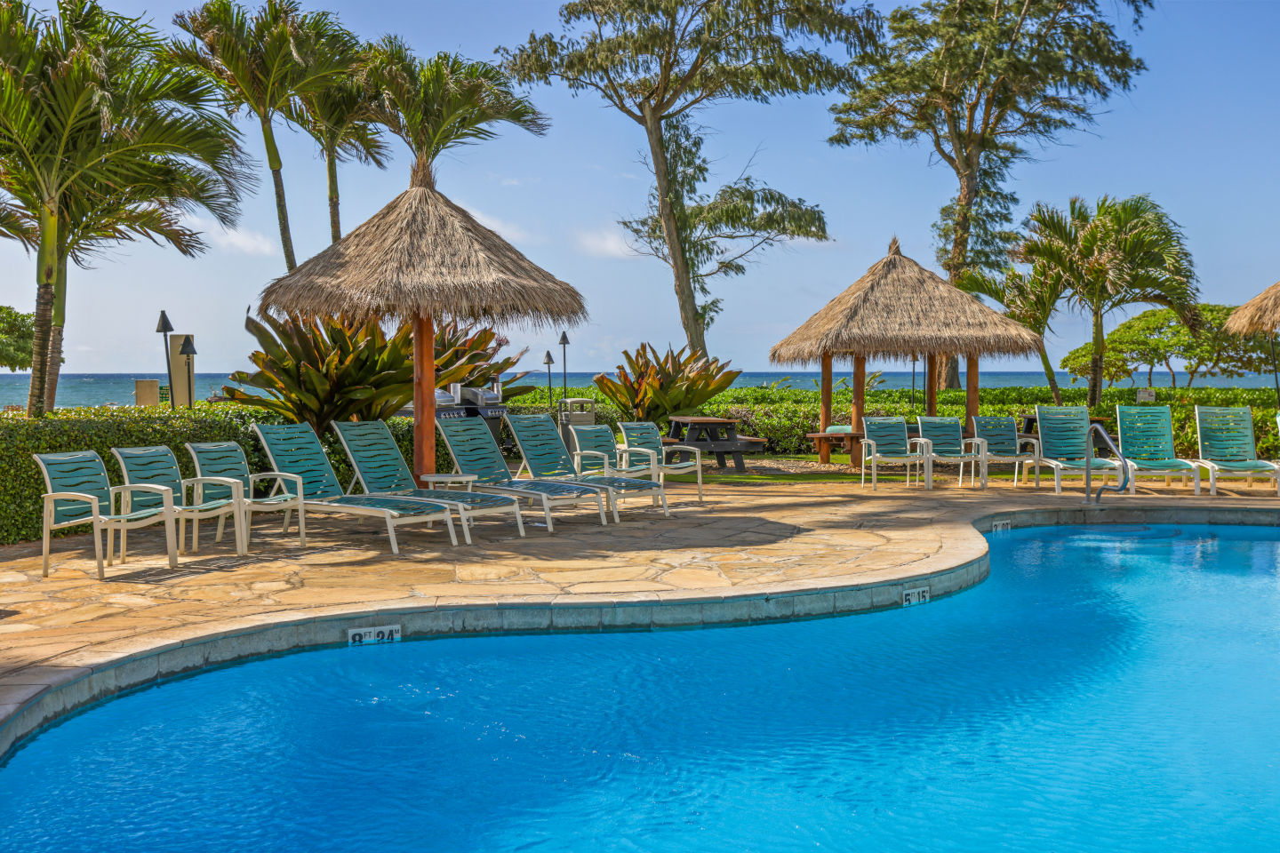 Pool and sun deck area with lounge chairs and the beach in the background.