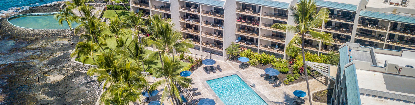 Drone view over the property capturing the resort's two pool, sand chair area, lawn and hotel near the shoreline