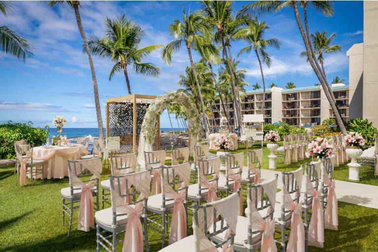 Wedding set up with chairs decorated with silk ribbons, floral archway facing the ocean at Aston Kona by the Sea