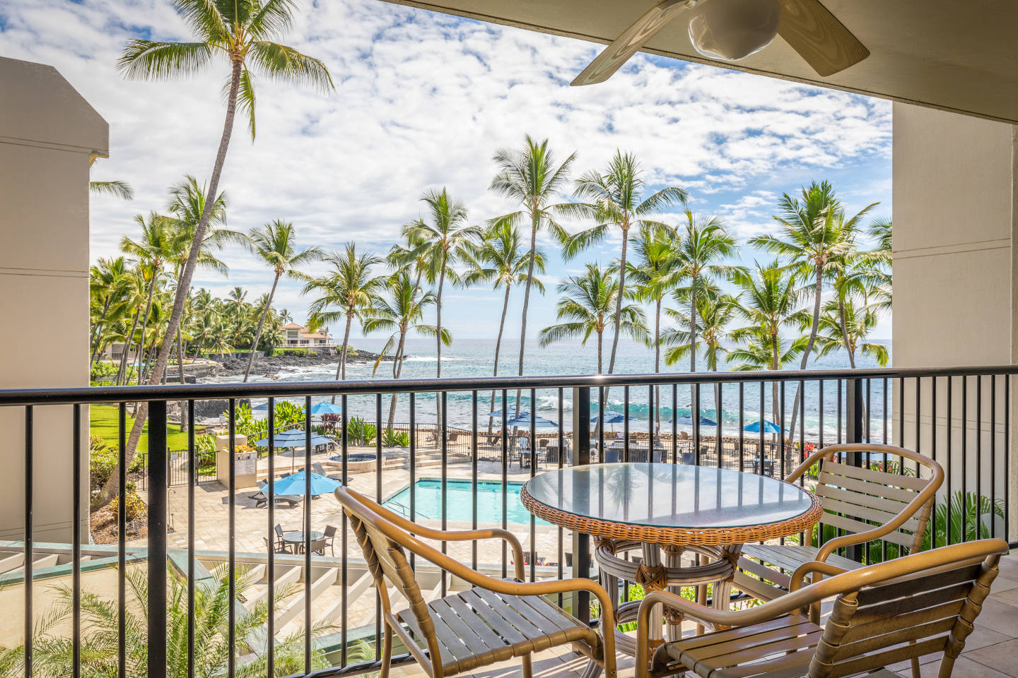 Balcony with glass table and chairs looking out to the pool and the ocean.