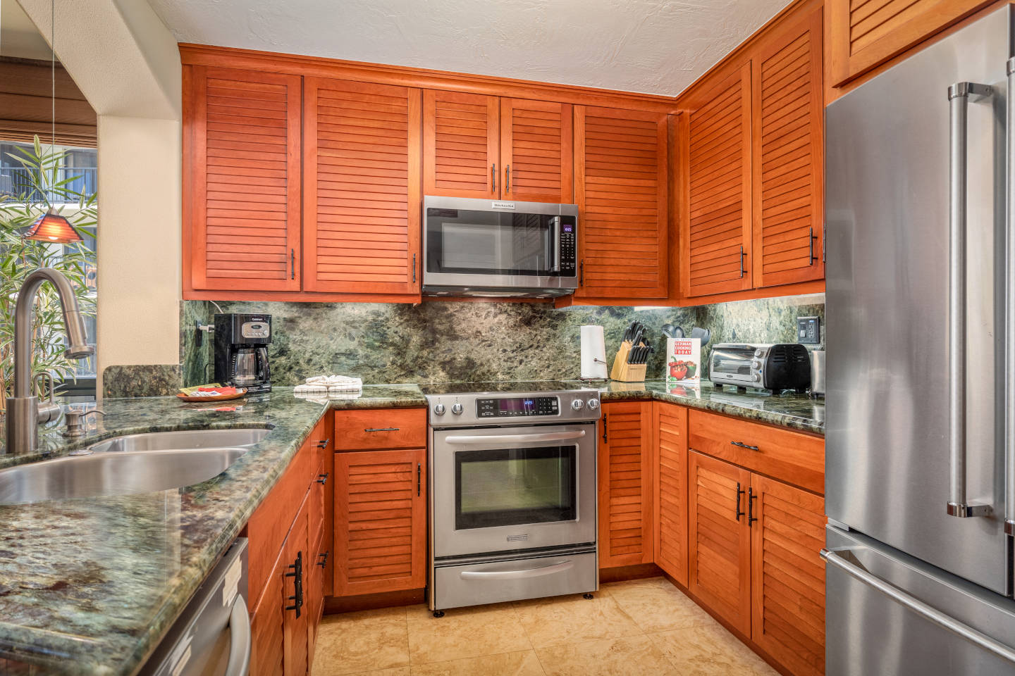 Updated kitchen with stove, oven, microwave, refrigerator, coffee maker, and toaster oven on marble countertop.