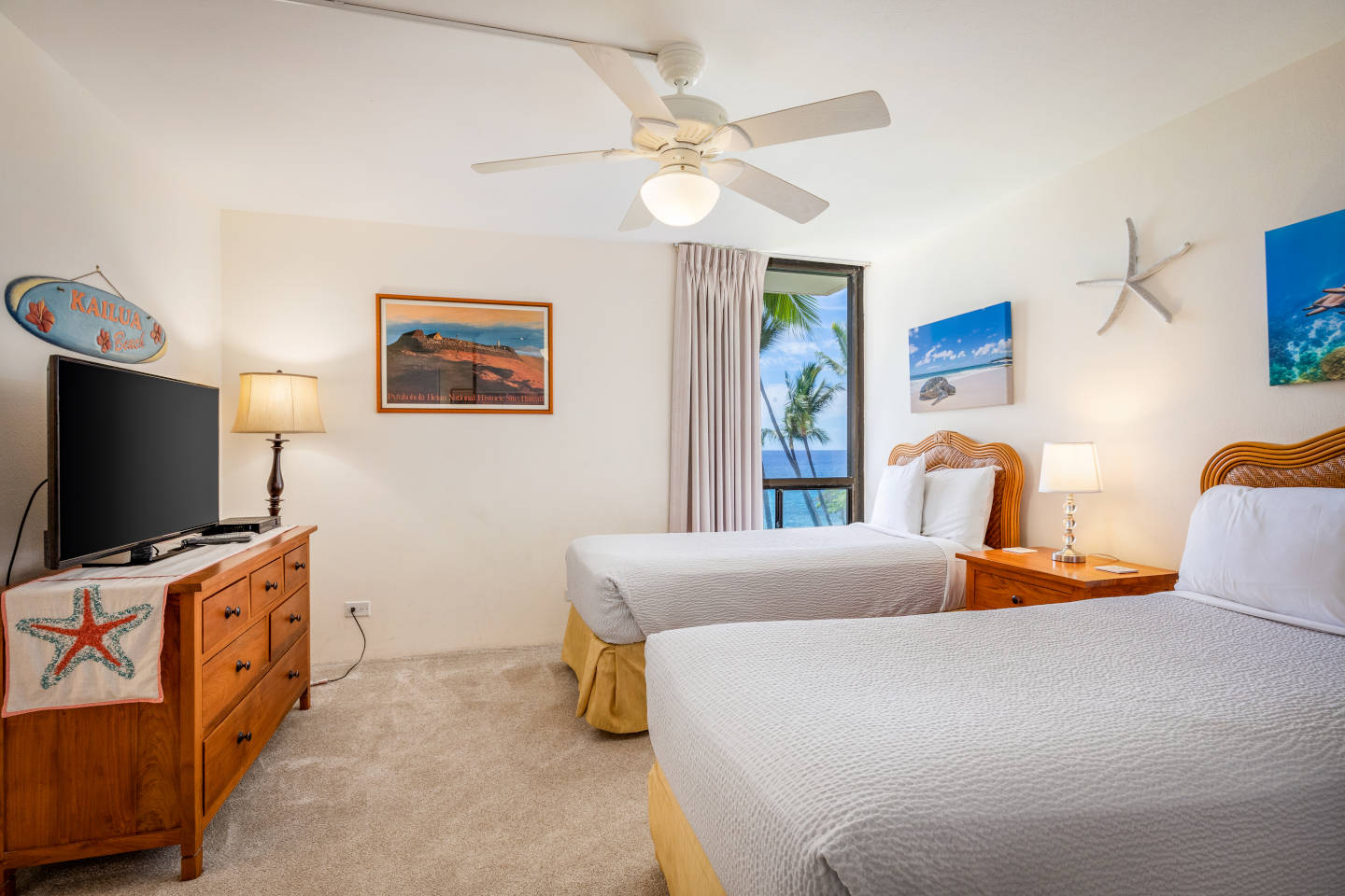 Room with 2 beds, lamps, TV, and a window overlooking to beach.