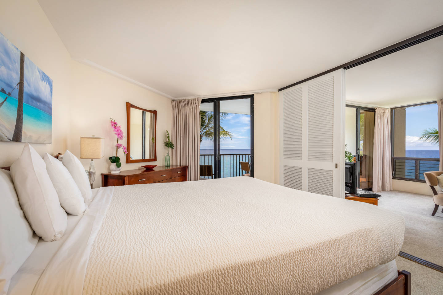 Room with king bed, dresser, balcony overlooking the ocean and sliding doors to living room.