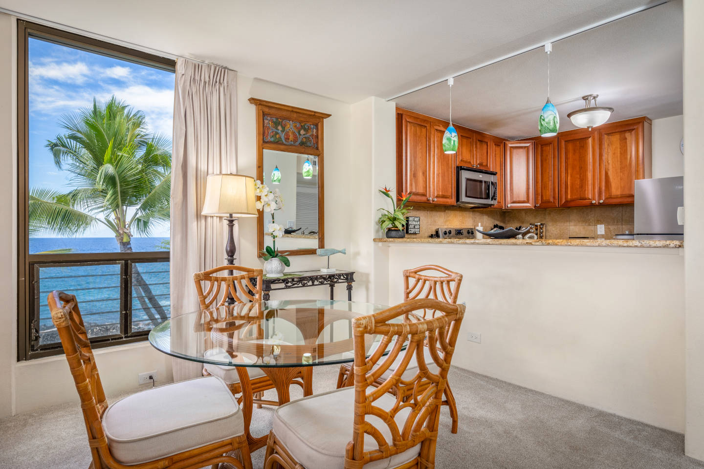 Dining area with table and chairs, balcony, and kitchen in background.