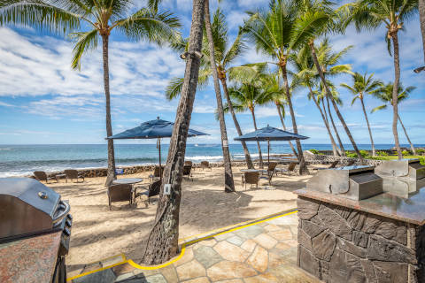 Sand area with beach chairs and umbrellas near the coastline with barbeque grills