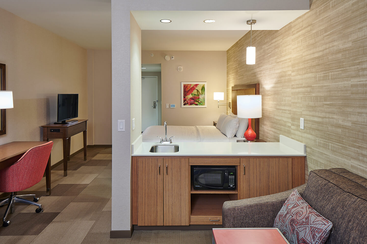 Room with couch, coffee table, lamp, desk, TV, microwave, semi-separate sleeping area