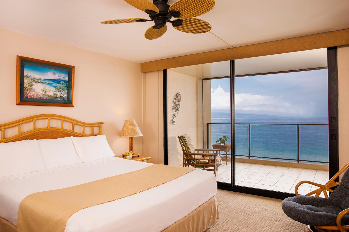 Room with a bed, nightstand, lamps, and balcony with oceanfront view.