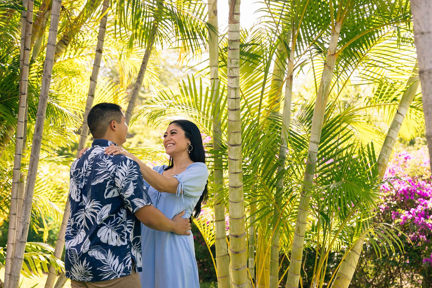Couple embracing beneath trees in resort gardens.