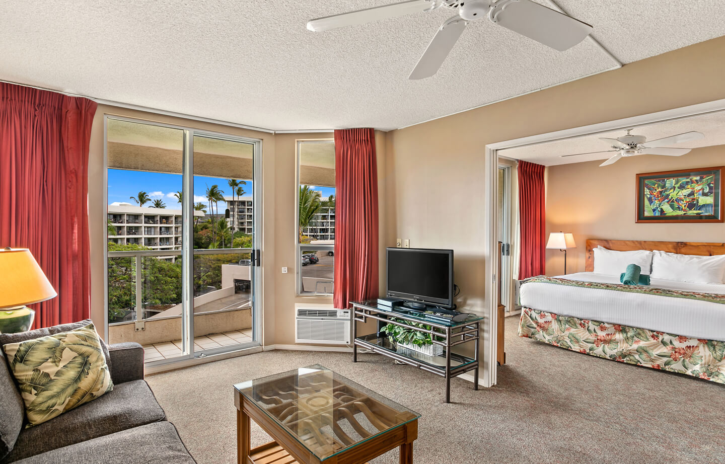 Living room with seating, coffee table, TV, balcony, doorway to bedroom.