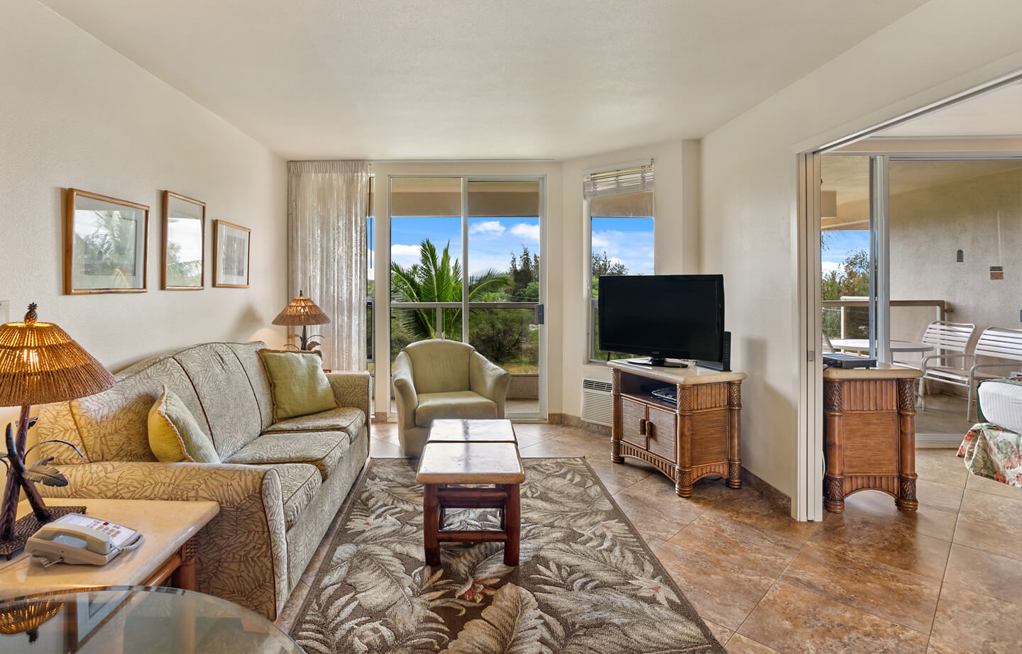 Living area with a couch, coffee table, TV, lamps, balcony, and entryway to bedroom.