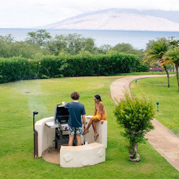 Mand and woman cooking at barbecue grill with resort and ocean views.