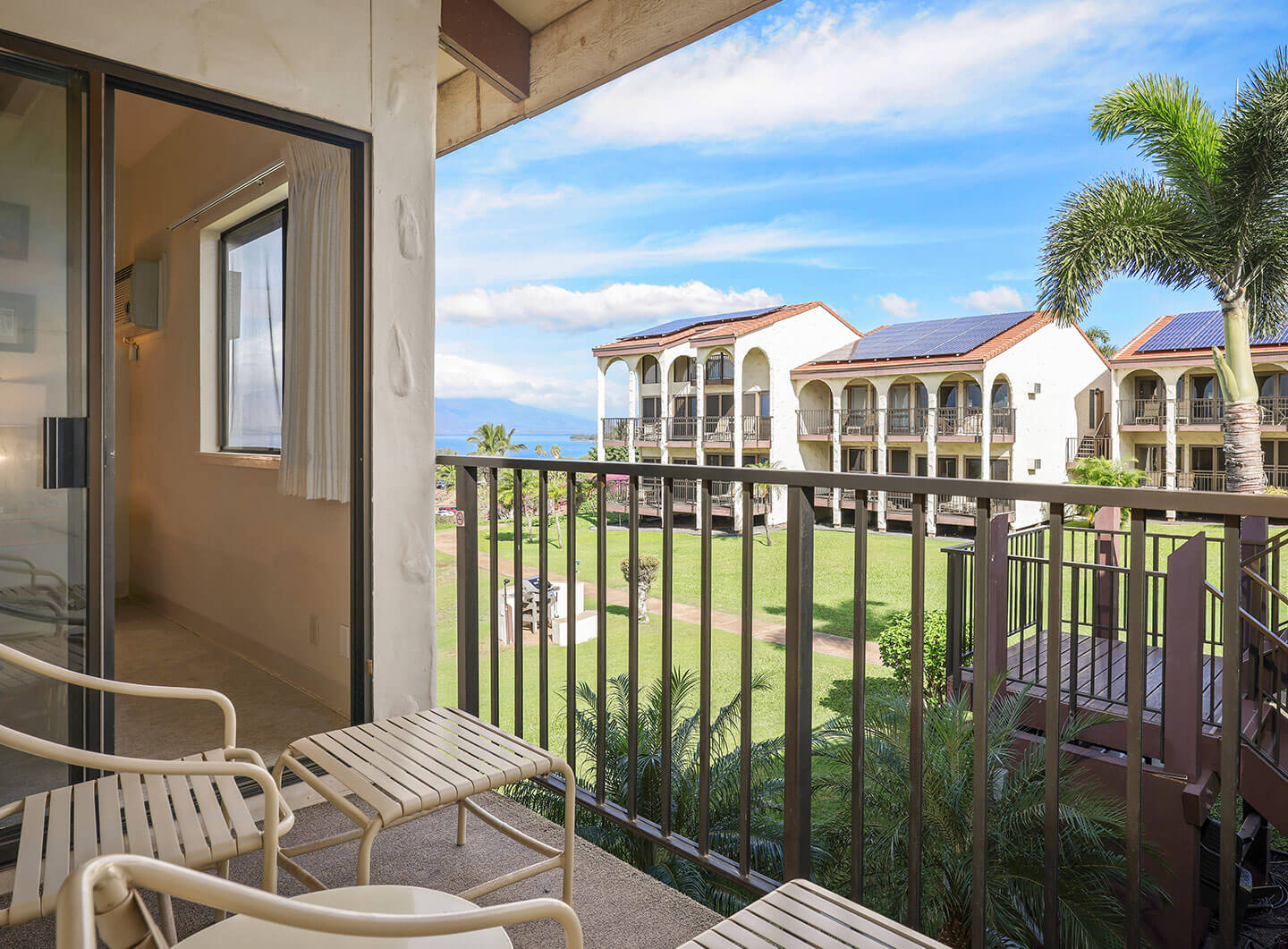 Balcony with chairs, table, and view of resort and ocean in the distance.