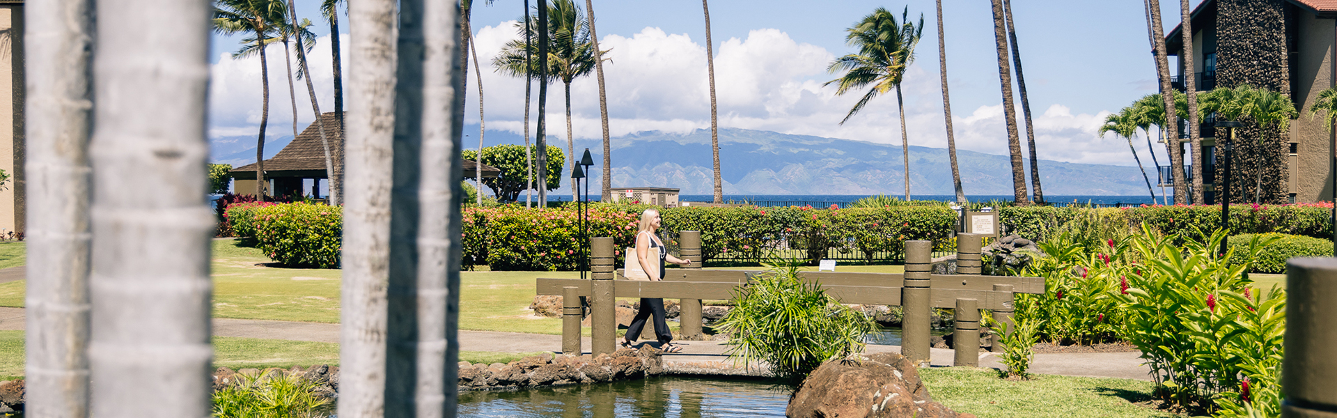 Woman walking through resort on wooden bridge over pond