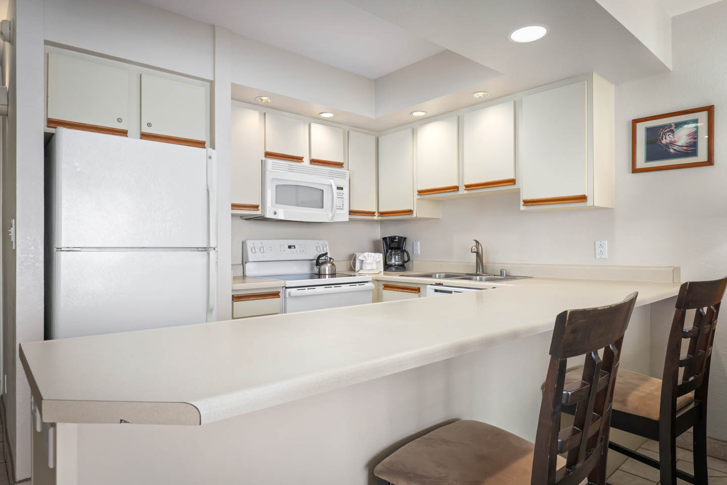 Kitchen with countertop seating, refrigerator, microwave.