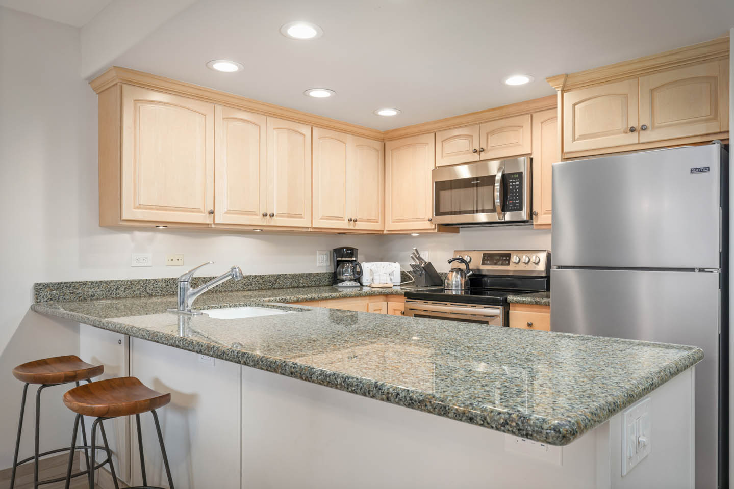 Kitchen with countertop seating, refrigerator, microwave, and stove.