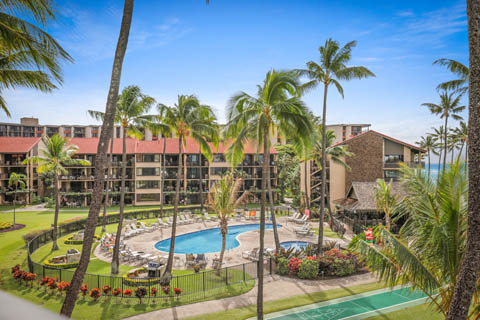 View of the grounds at Aston at Papakea Resort with pool, barbecue grills, and palm trees