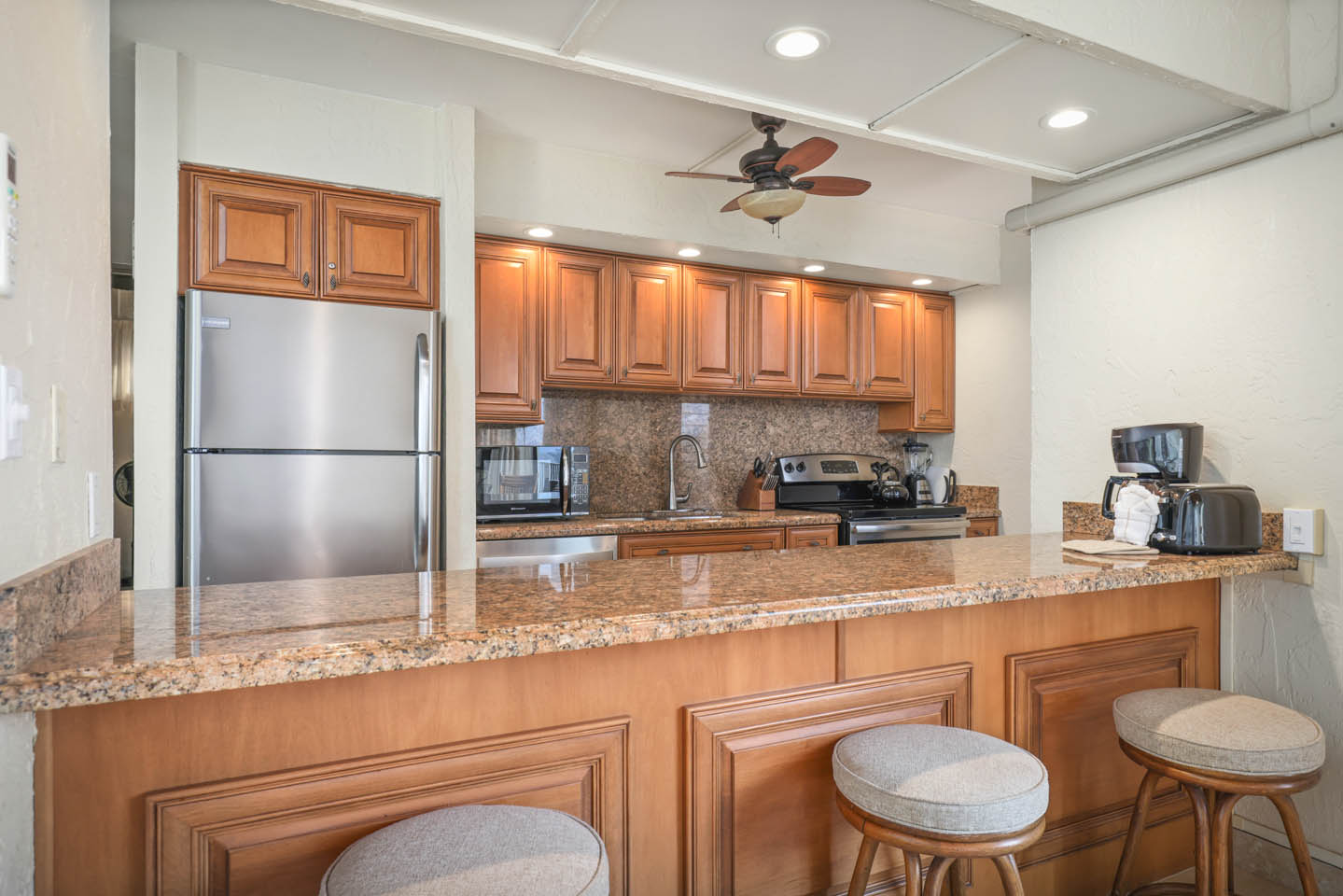 Kitchen with countertop seating, a refrigerator, microwave, and stove.