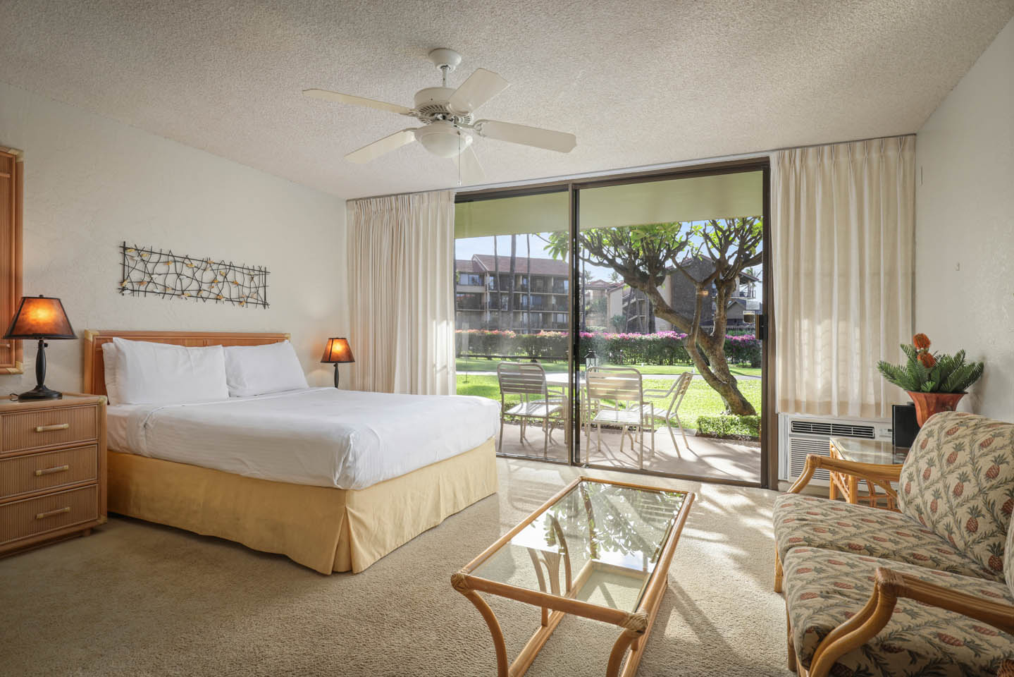 Room with a bed, nightstand, couch, coffee table, lamps, and patio.