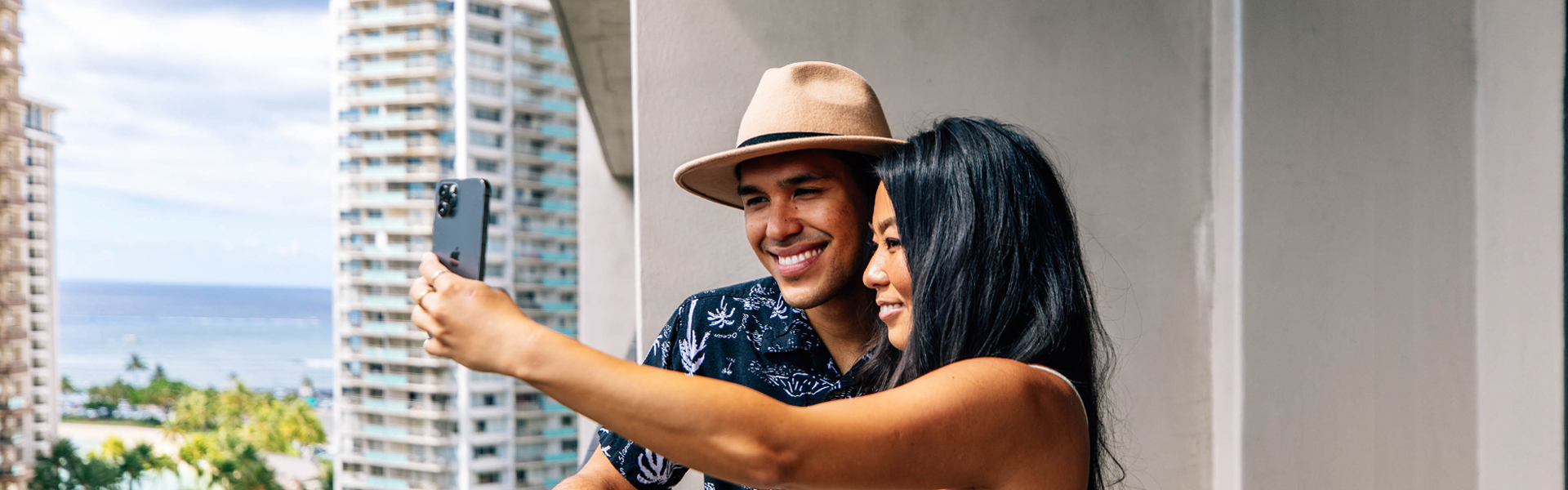 Couple taking selfie with phone on lanai with views of Waikiki