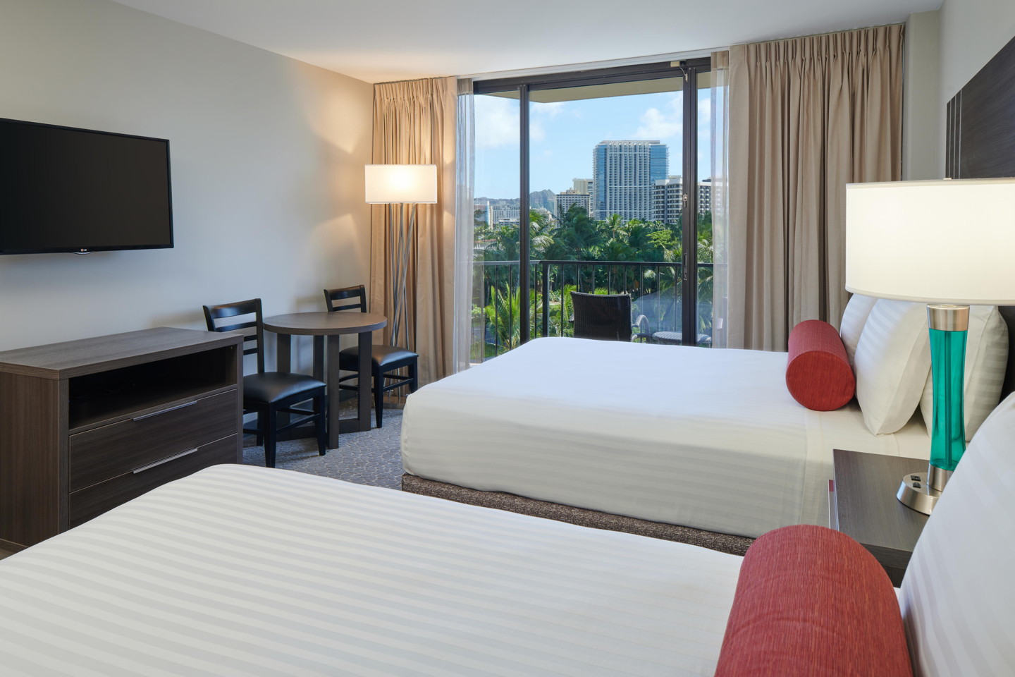 Room with 2 beds, nightstand, lamps, dresser, table, chairs, TV, and balcony.