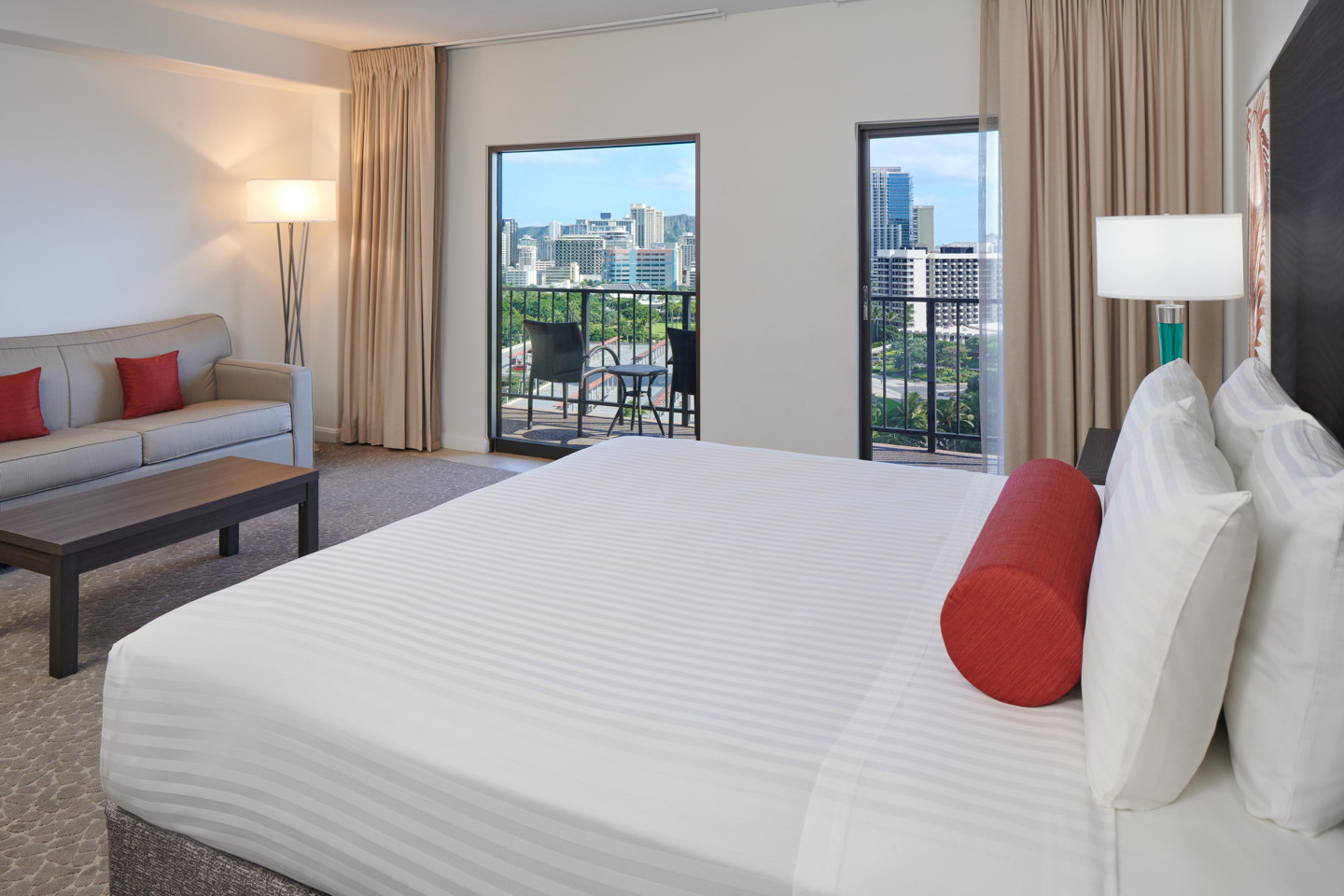 Room with a bed, couch, coffee table, lamp, balcony.
